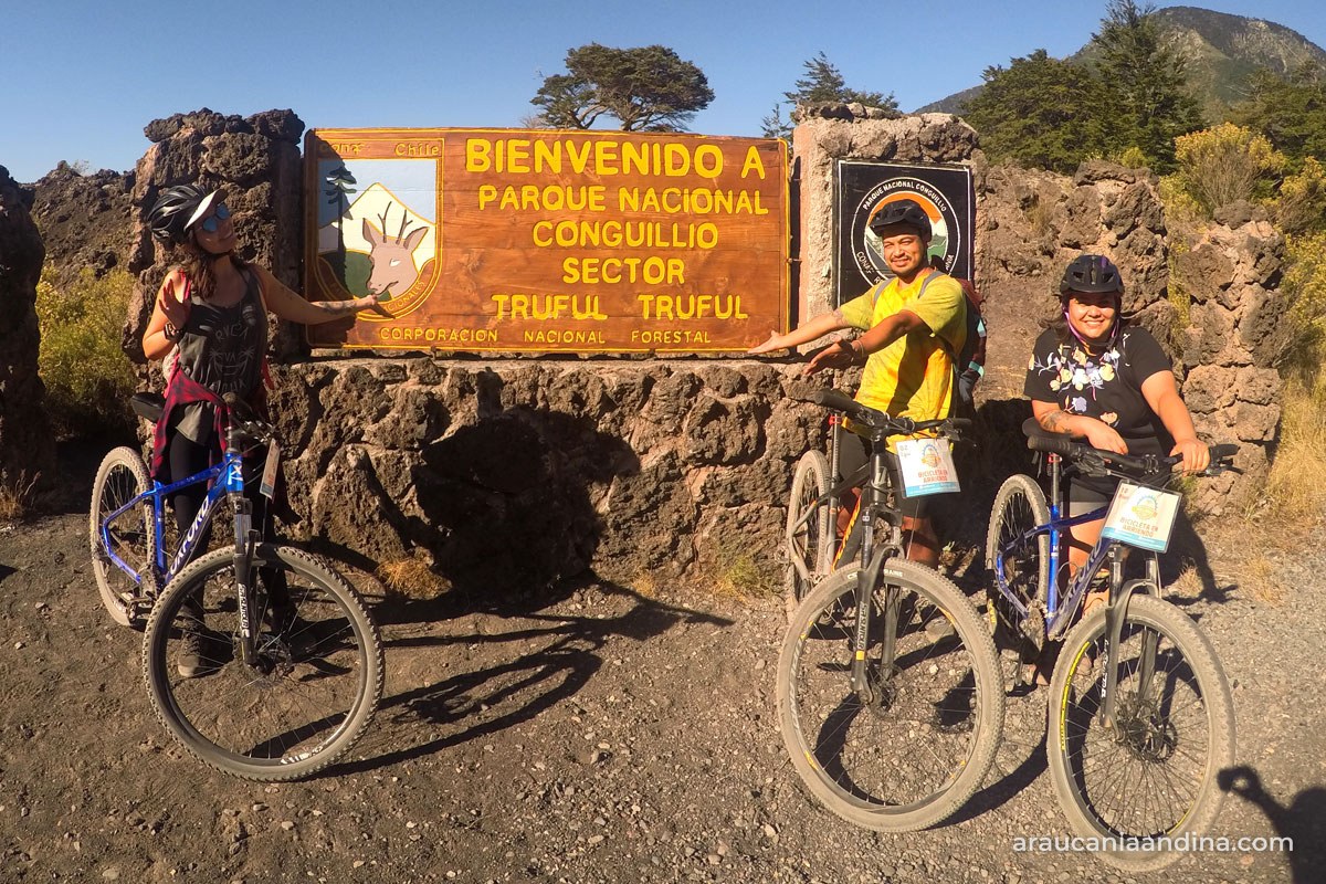 Ciclistas de un tour de Melibike junto al letrero del Parque Nacional Conguillío, sector Truful Truful