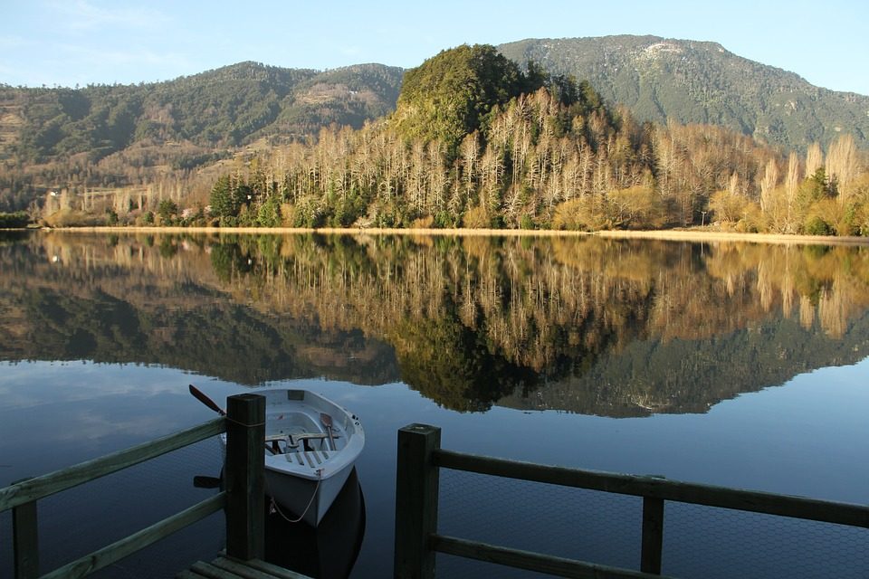 Laguna Acanpulli de aguas quietas que reflejan el bosque, con un bote junto al muelle